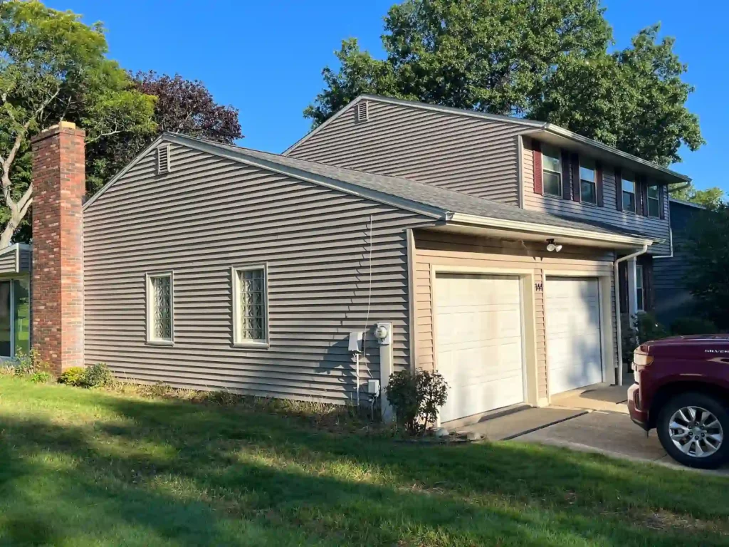 picture of a home from the side of the driveway with new siding that was just installed. you can see the garage doors too.